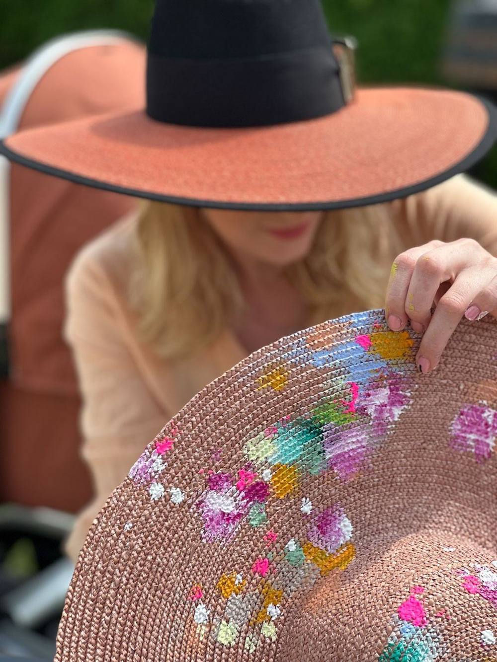 Juliane Golbs hält einen von ihr mit bunten Blüten bemalten Strohhut, im Hintergrund trägt sie selbst einen breitkrempigen Hut