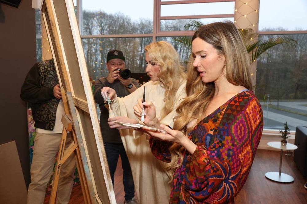 Juliane Golbs und Joss Stone stehen mit Pinsel und Palette an einer großen Leinwand auf der Staffelei, im Hintergrund ein Fotograf