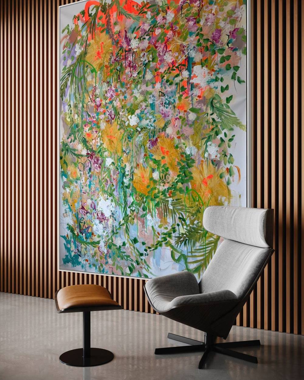 Großformatiges florales Gemälde von Juliane Golbs vor einer Wand aus Holzlamellen, davor ein grauer Lounge-Sessel