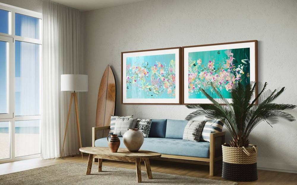 Zwei türkisfarbene florale Gemälde von Juliane Golbs gerahmt über einem Sofa in einem hellen Raum mit Blick aufs Meer