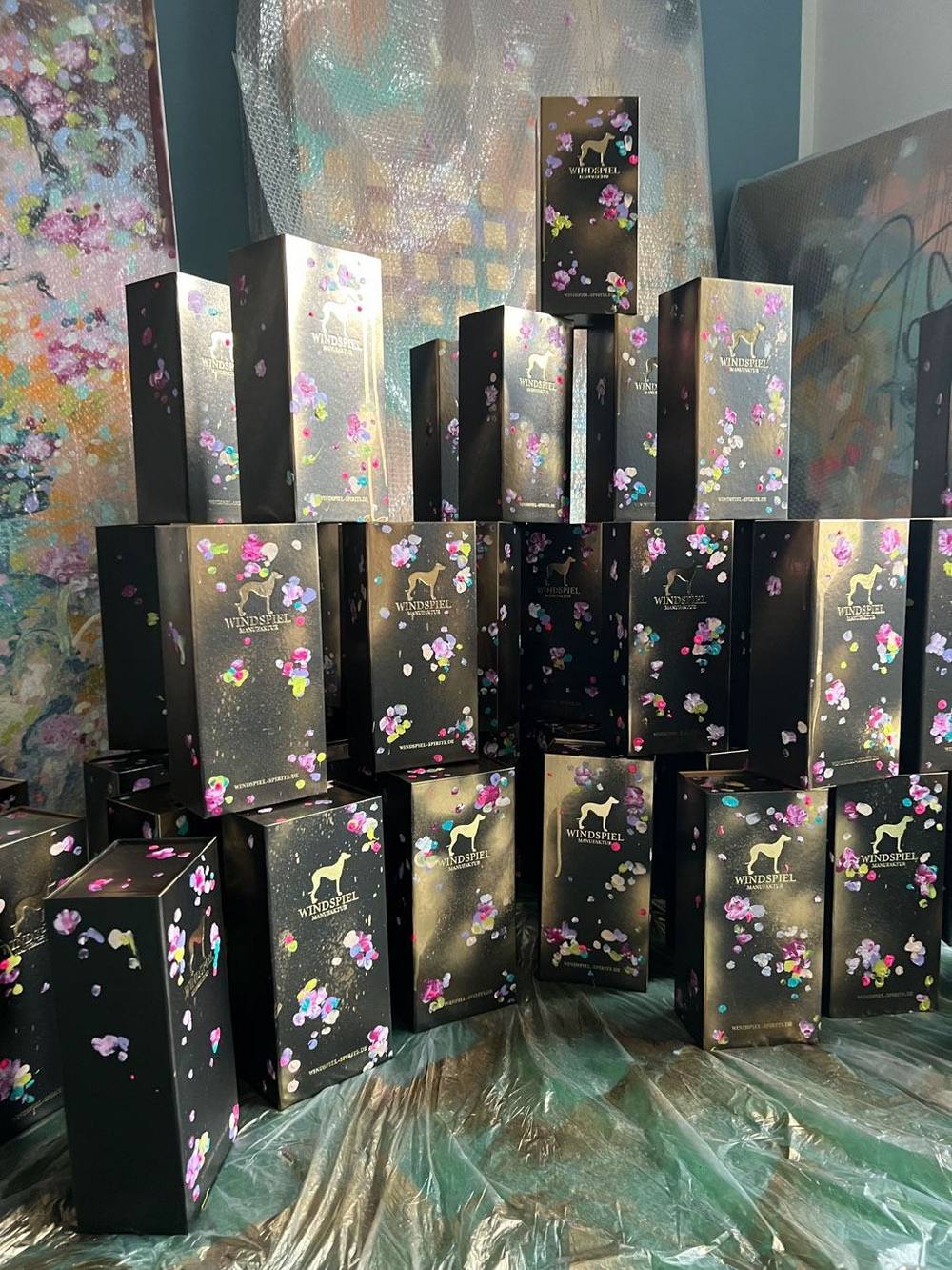 Gestapelte schwarze Verpackungen der Windspiel Art Edition mit floralen Farbakzenten im Atelier von Juliane Golbs